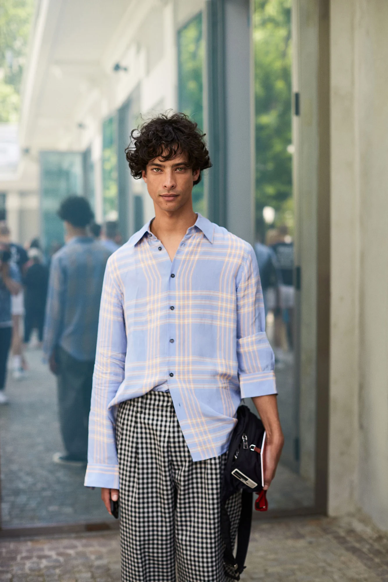 Curly-haired man in a pale blue plaid shirt and black-and-white gingham trousers on a city street, for The Sartorialist.