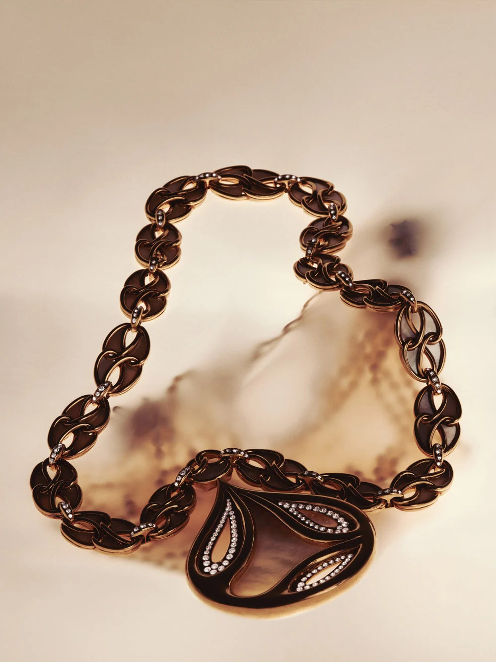 Rose gold chain-link necklace with brown enamel and diamond-set teardrop pendant on a cream surface, for Marie Claire.
