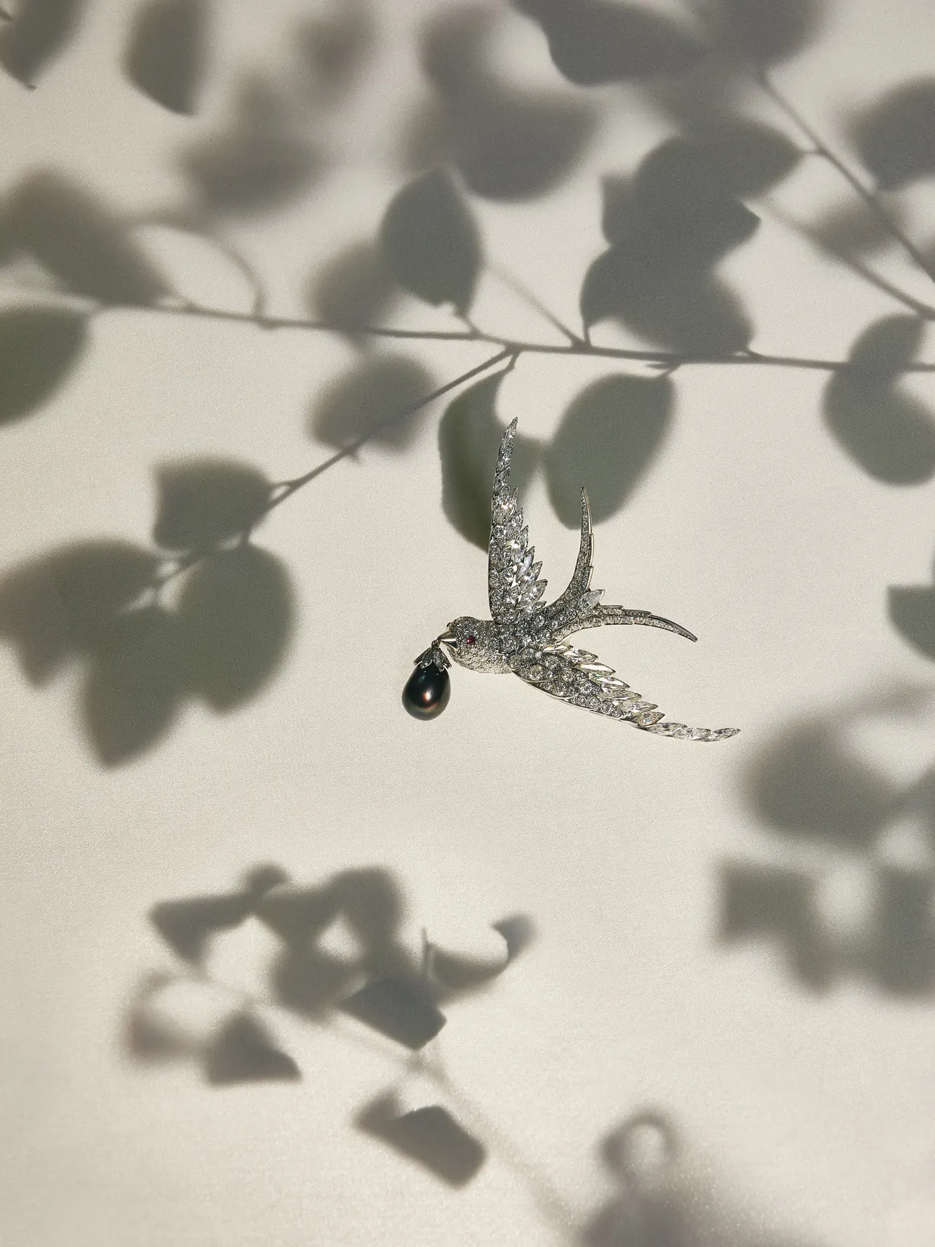 Diamond swallow brooch holding a black pearl drop, set on cream with leaf shadows, for Marie Claire.