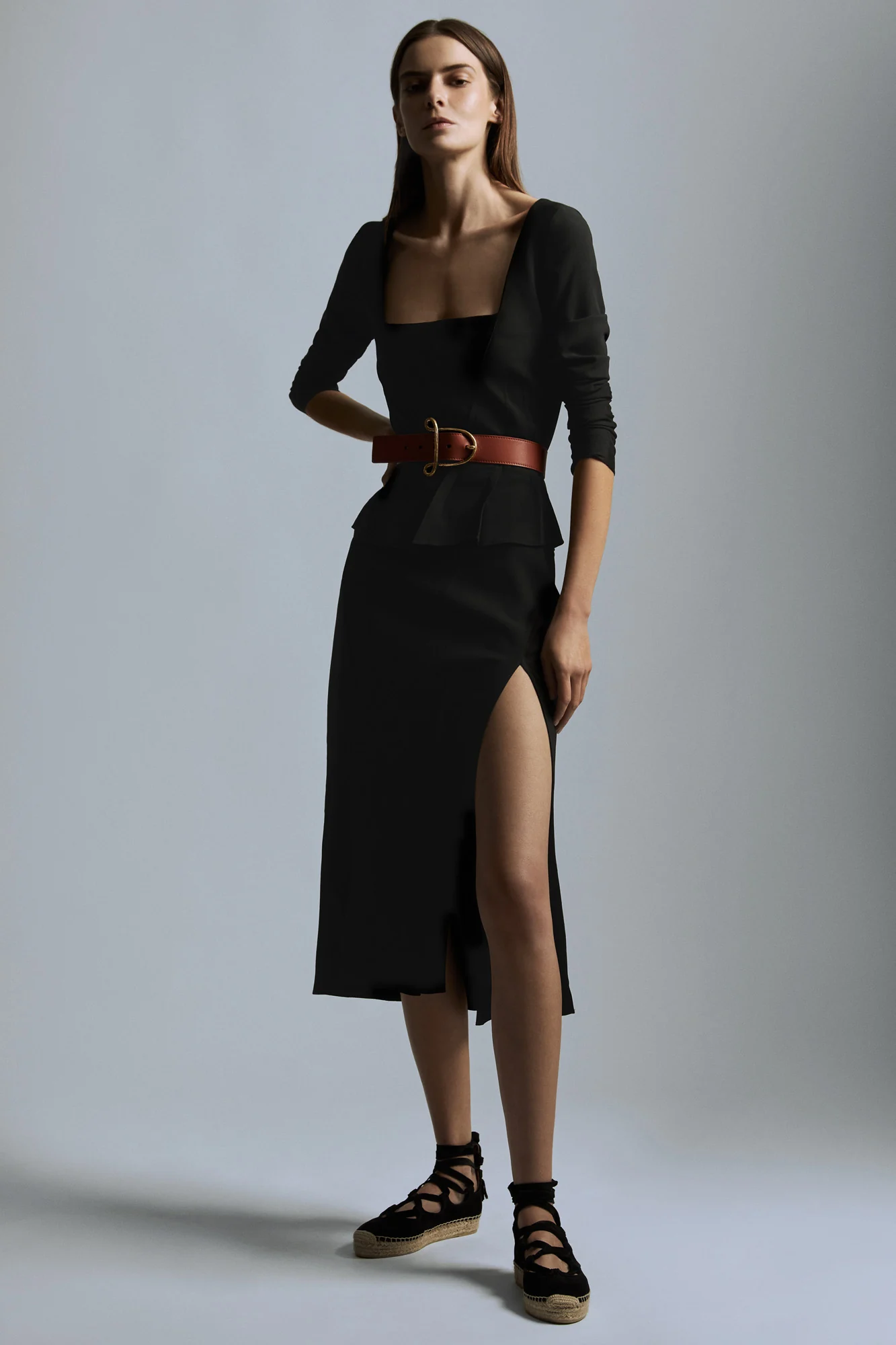 Model in a black square-neck top, high-slit skirt, brown leather belt and lace-up espadrilles on grey, for Altuzarra.