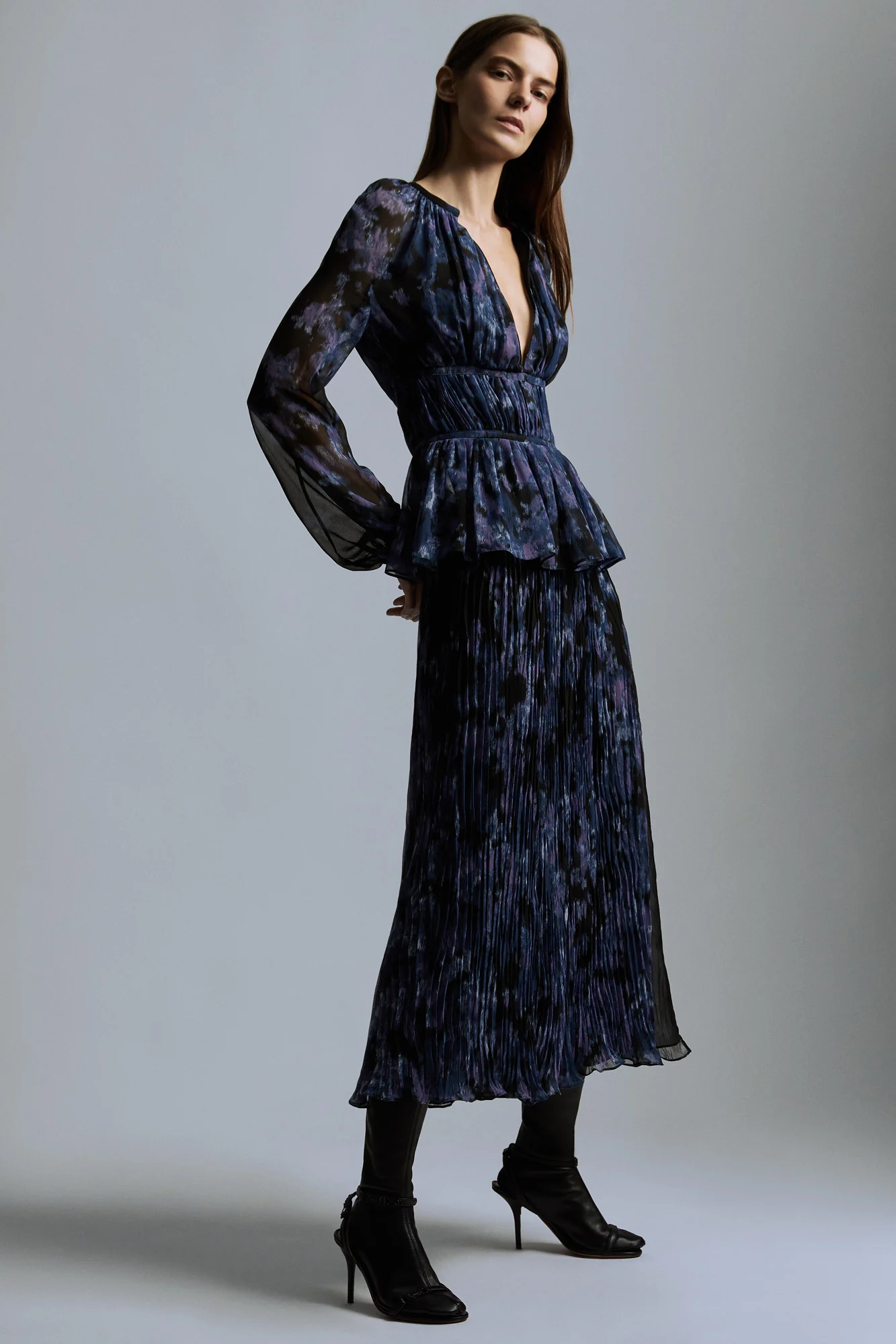 Model in a long-sleeve navy floral chiffon peplum dress with pleated skirt and black heels on grey, for Altuzarra.