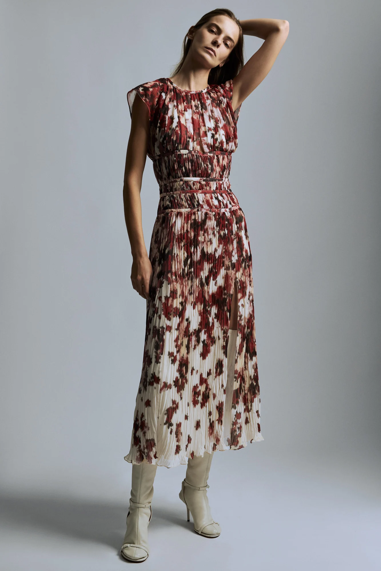 Model in a pleated red and ivory floral midi dress with cream heeled boots against a grey backdrop, for Altuzarra.