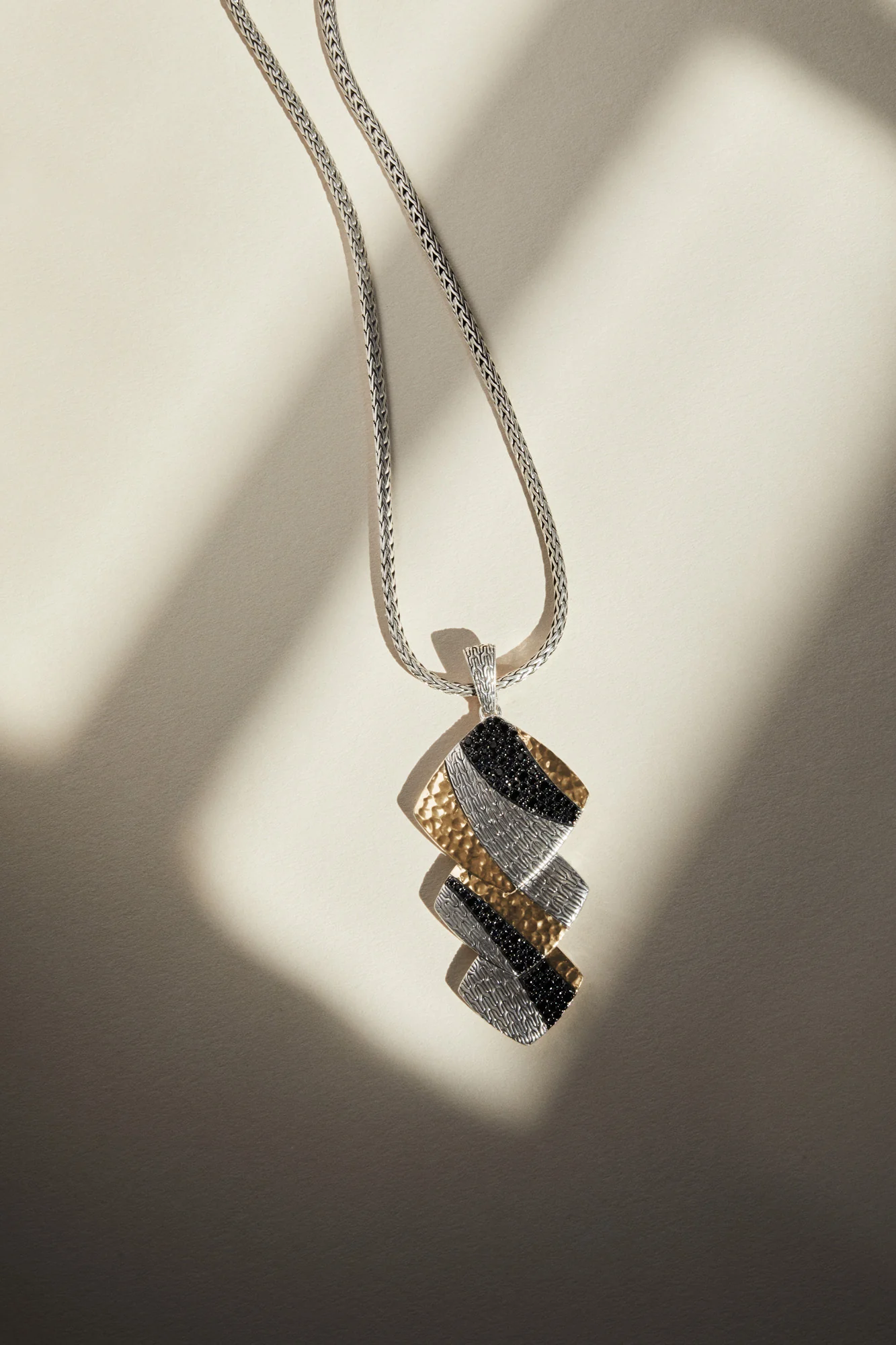 Silver chain necklace with tiered hammered gold and silver pendant set with black sapphires, in window light, for John Hardy.