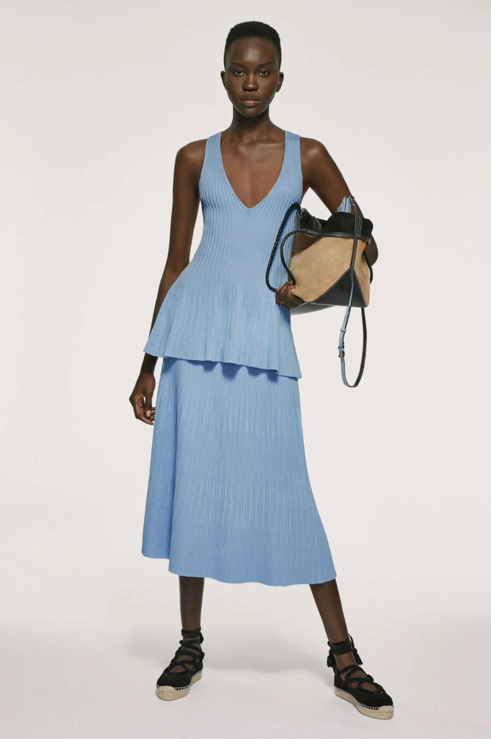 Model in a blue ribbed knit peplum top and midi skirt with a suede tote and espadrilles, for Altuzarra.