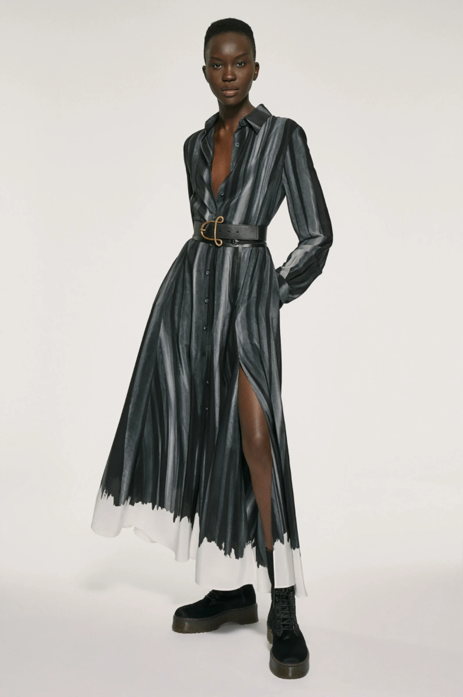 Model in a grey and black striped belted shirt dress with dip-dyed white hem and black boots, for Altuzarra.
