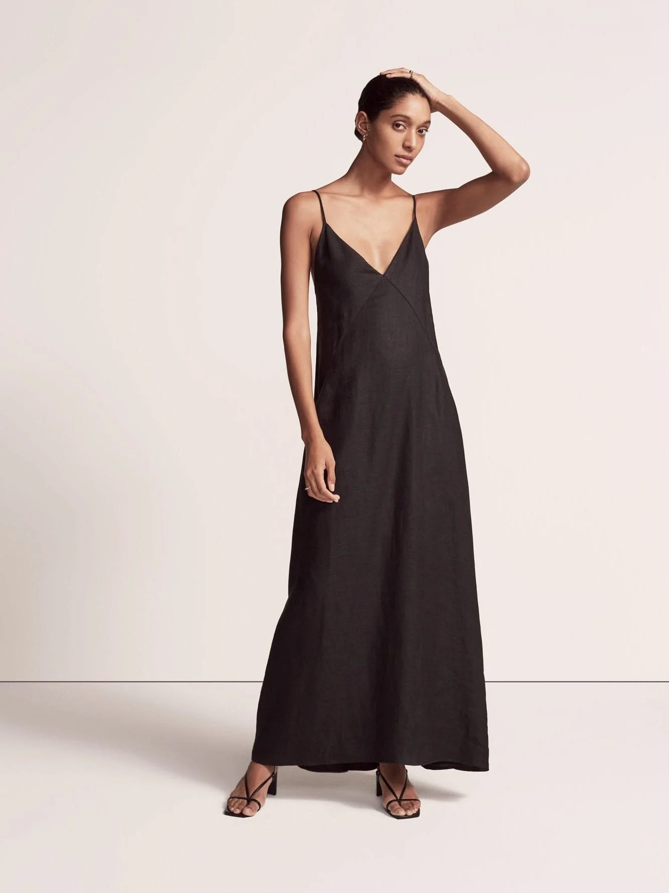 Model in a black linen maxi slip dress and strappy black sandals against a plain studio backdrop, for Another Tomorrow.