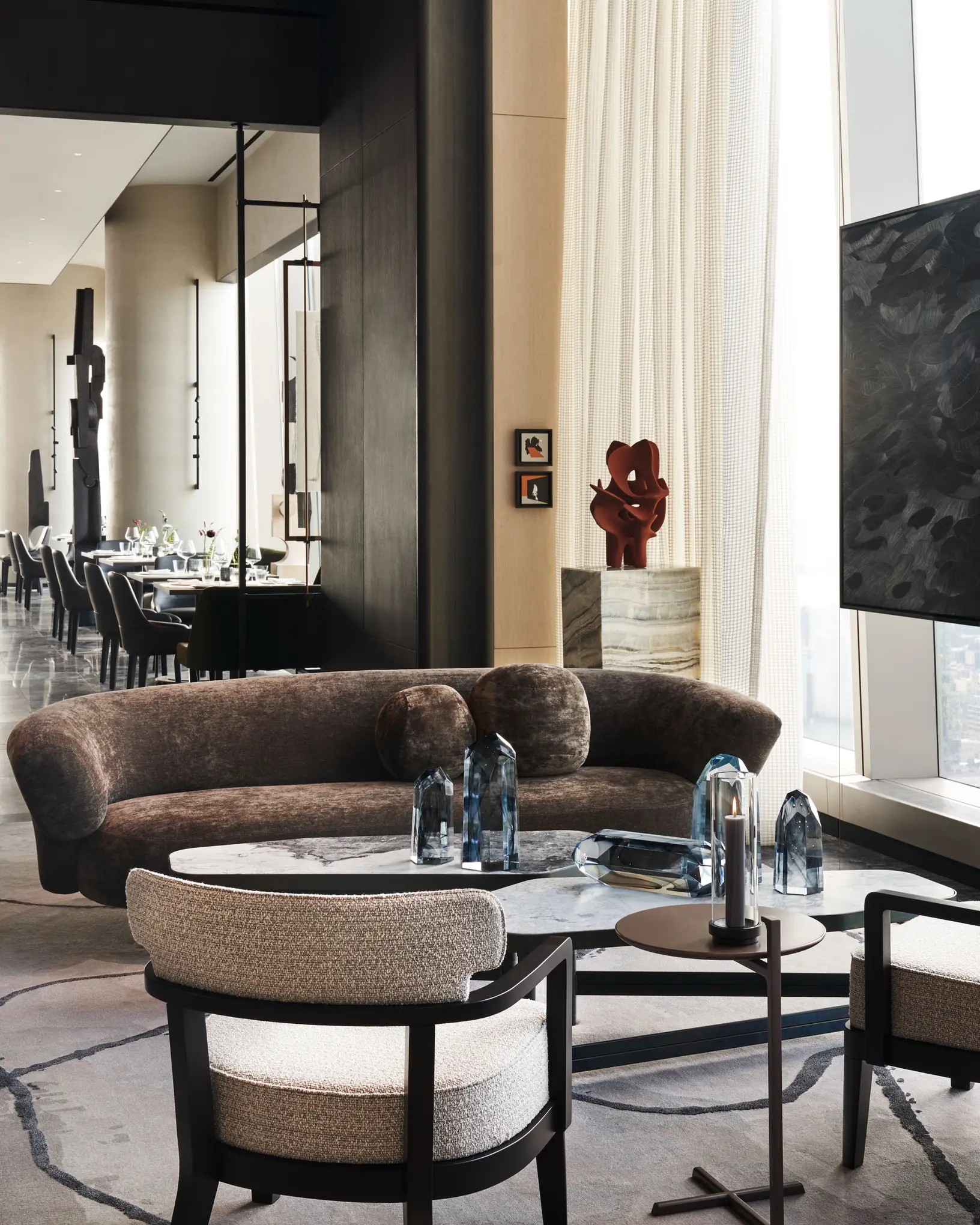 Lounge with a curved brown velvet sofa, marble coffee table, blue crystal decor and dining room beyond, for Centurion New York.