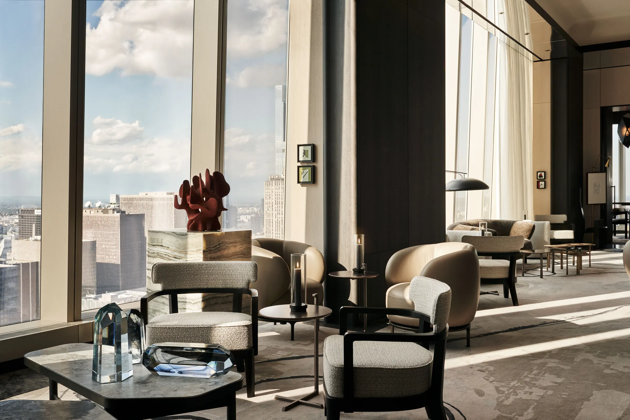 Hotel lounge with bouclé armchairs, red coral sculpture and floor-to-ceiling windows over the skyline, for Centurion New York.