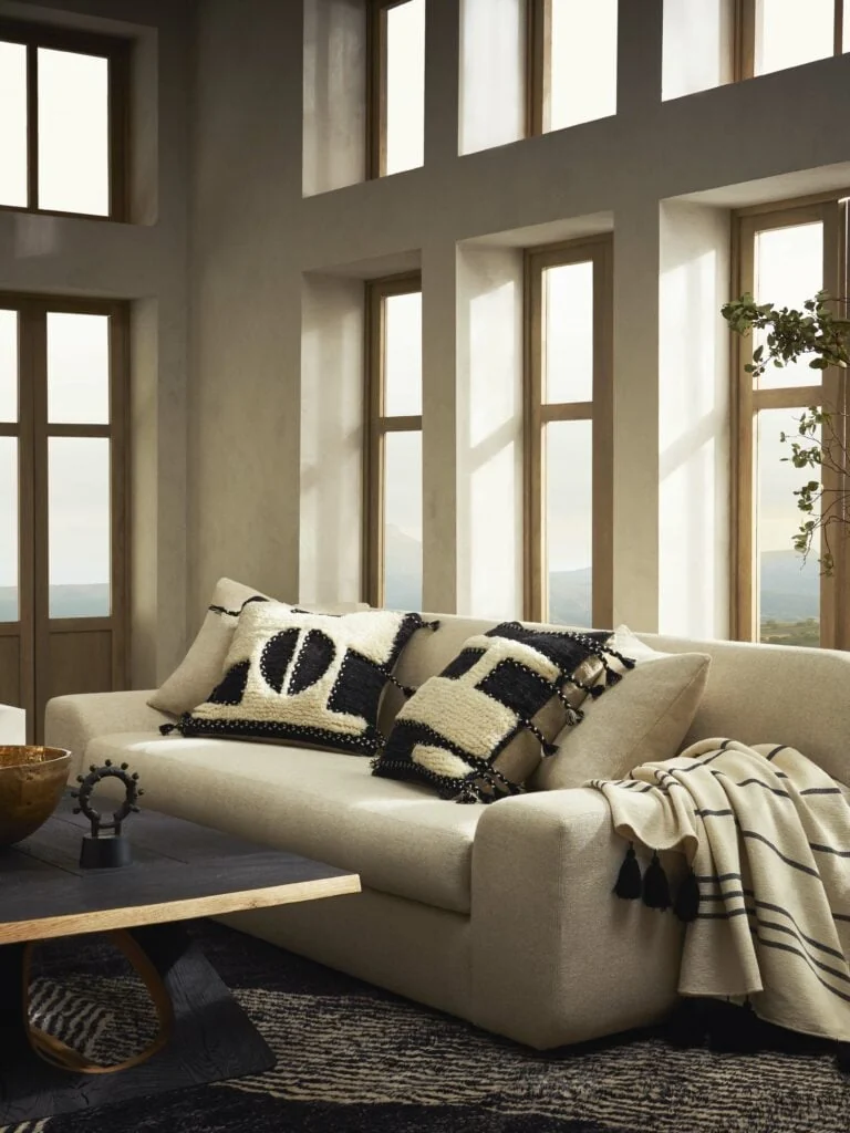 Cream sofa with black-and-white tufted pillows and striped throw in a sunlit room with tall windows, for Banana Republic.