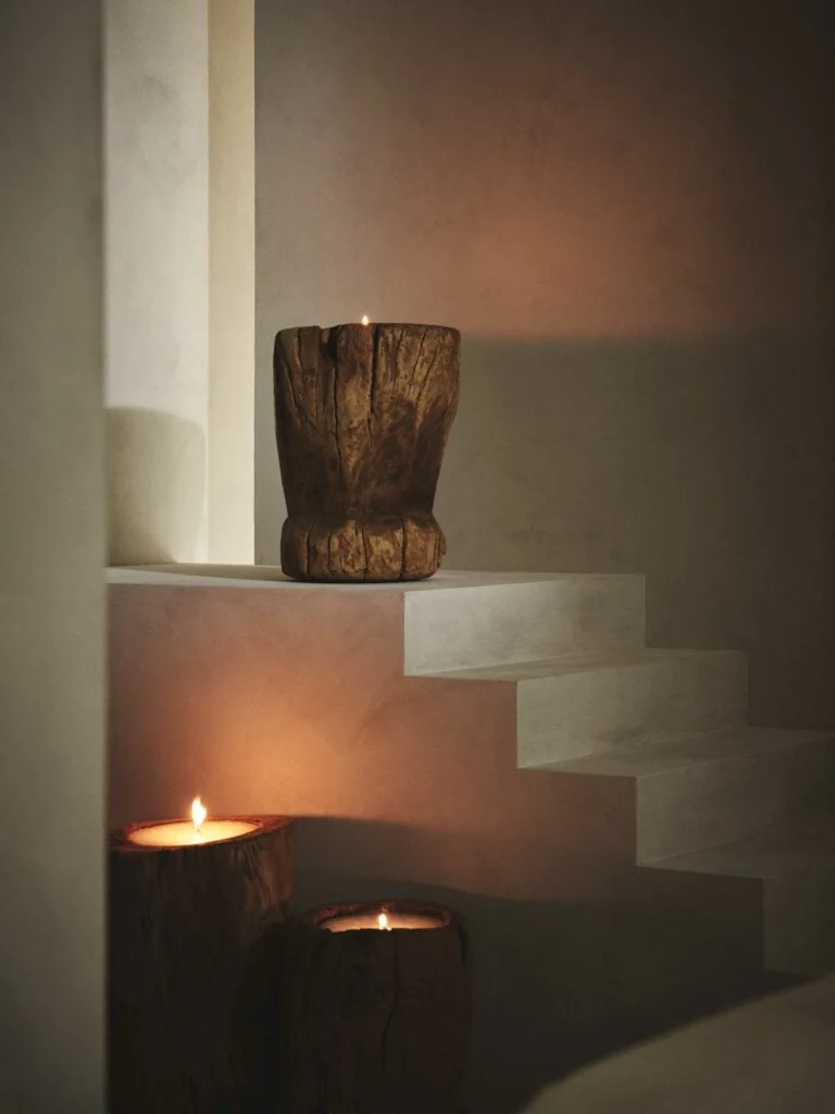 Lit candles in carved wooden vessels on white plaster steps in warm low light, for Banana Republic.