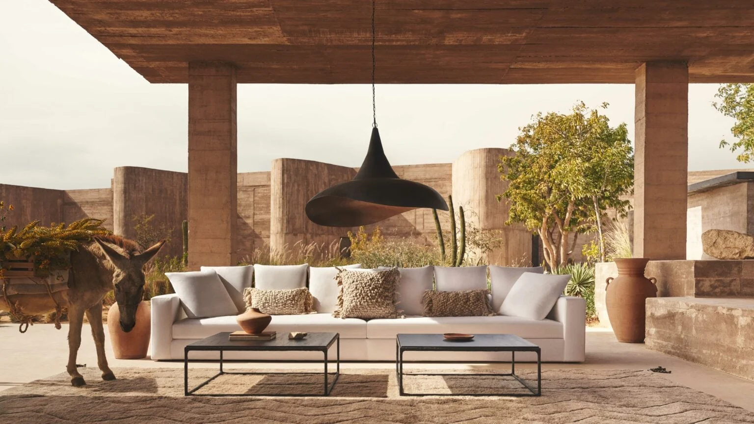 Covered concrete terrace with white sofa, black pendant lamp, steel coffee tables and a donkey in Mexico, for Banana Republic.