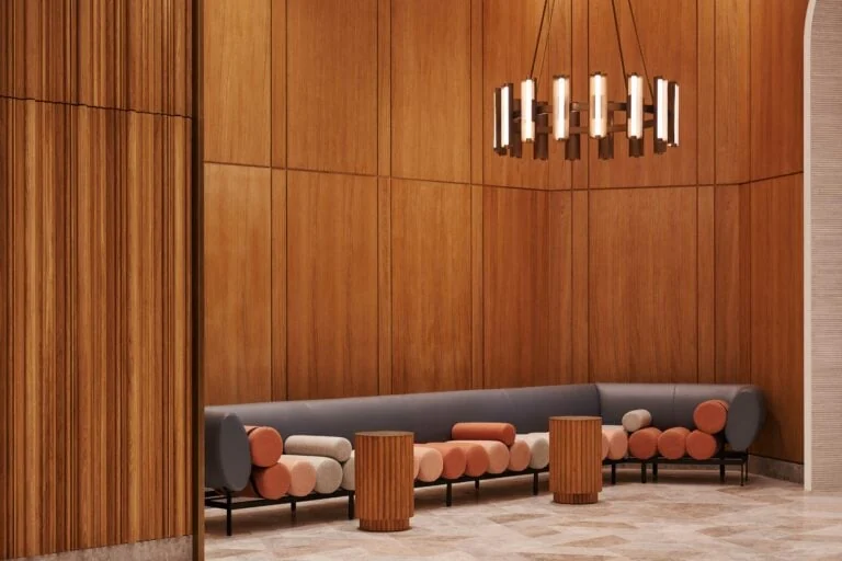 Lobby lounge with wood-paneled walls, grey curved sofa with orange cylinder cushions and a ring chandelier, for Brooklyn Tower.