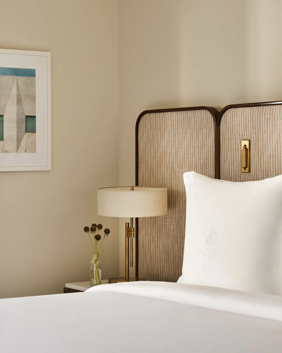 Hotel bed with embroidered white pillow, woven cane headboard, brass lamp and thistle vase, for Four Seasons.