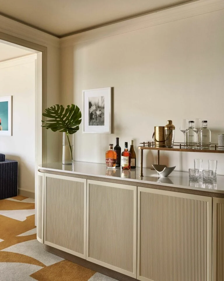 Hotel suite bar with fluted cream credenza, liquor bottles, brass tray and monstera leaf in a vase, for Four Seasons.
