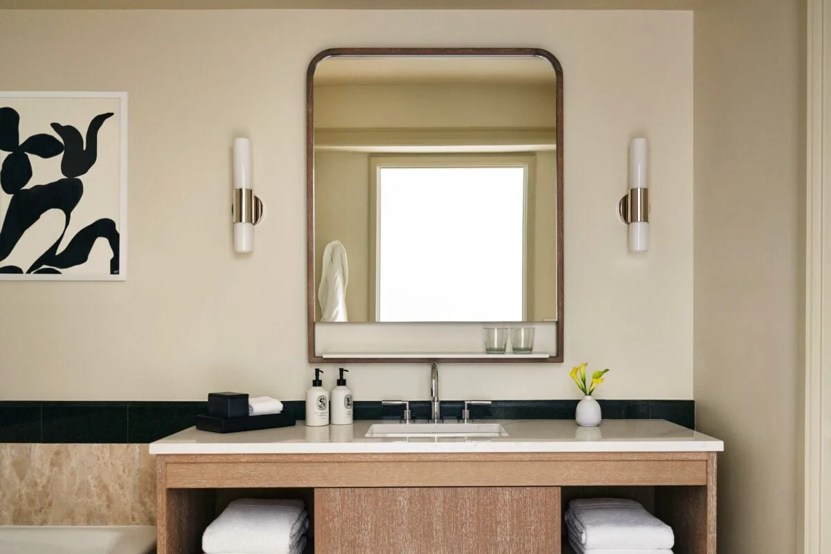 Hotel bathroom vanity with arched mirror, twin wall sconces, white towels and abstract black artwork, for Four Seasons.