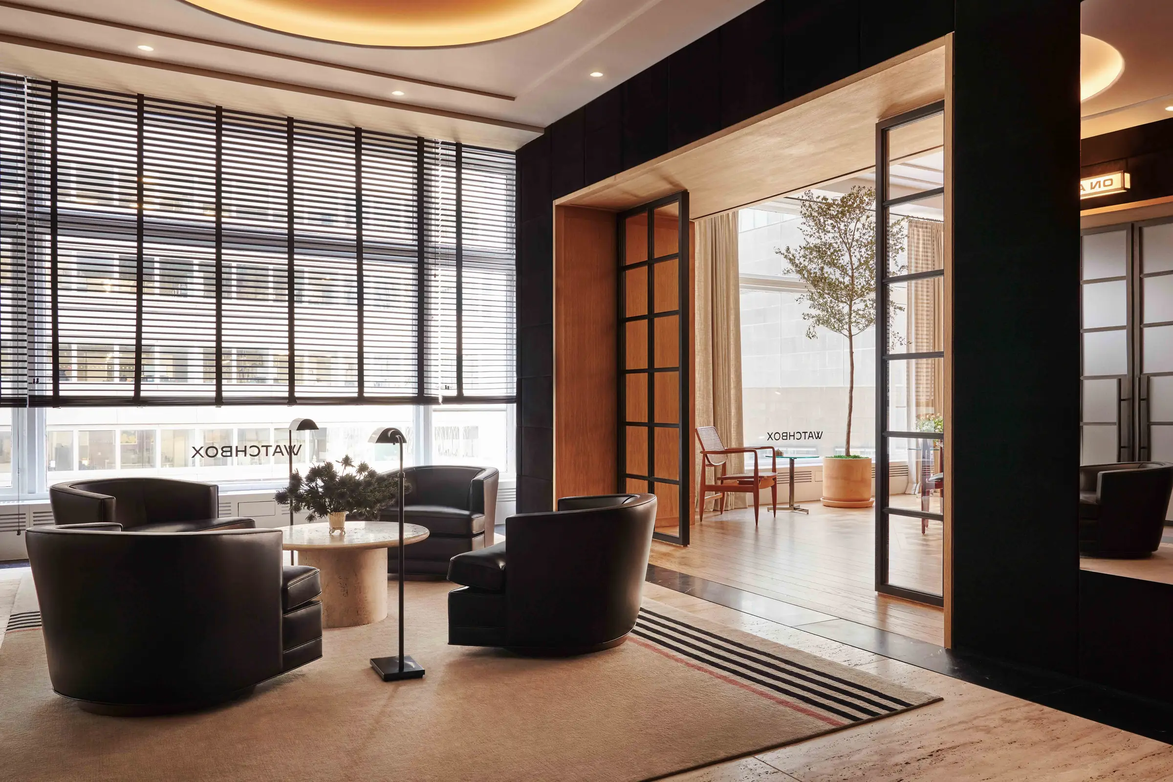 Showroom lounge with black leather swivel chairs, round stone table and framed glass doors to a sunlit room, for WatchBox.