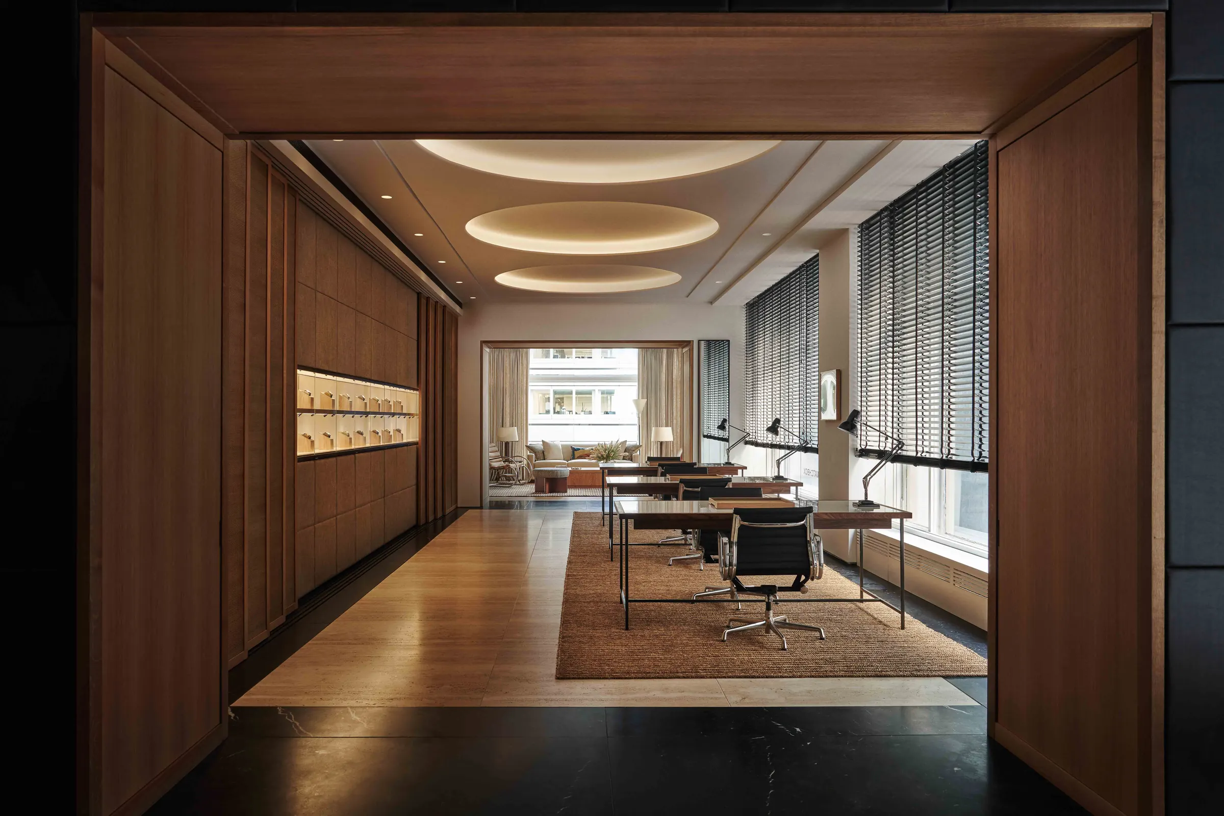Interior with wood-paneled walls, cove-lit ceiling, desks with black lamps on a jute rug and lit display niches, for WatchBox.