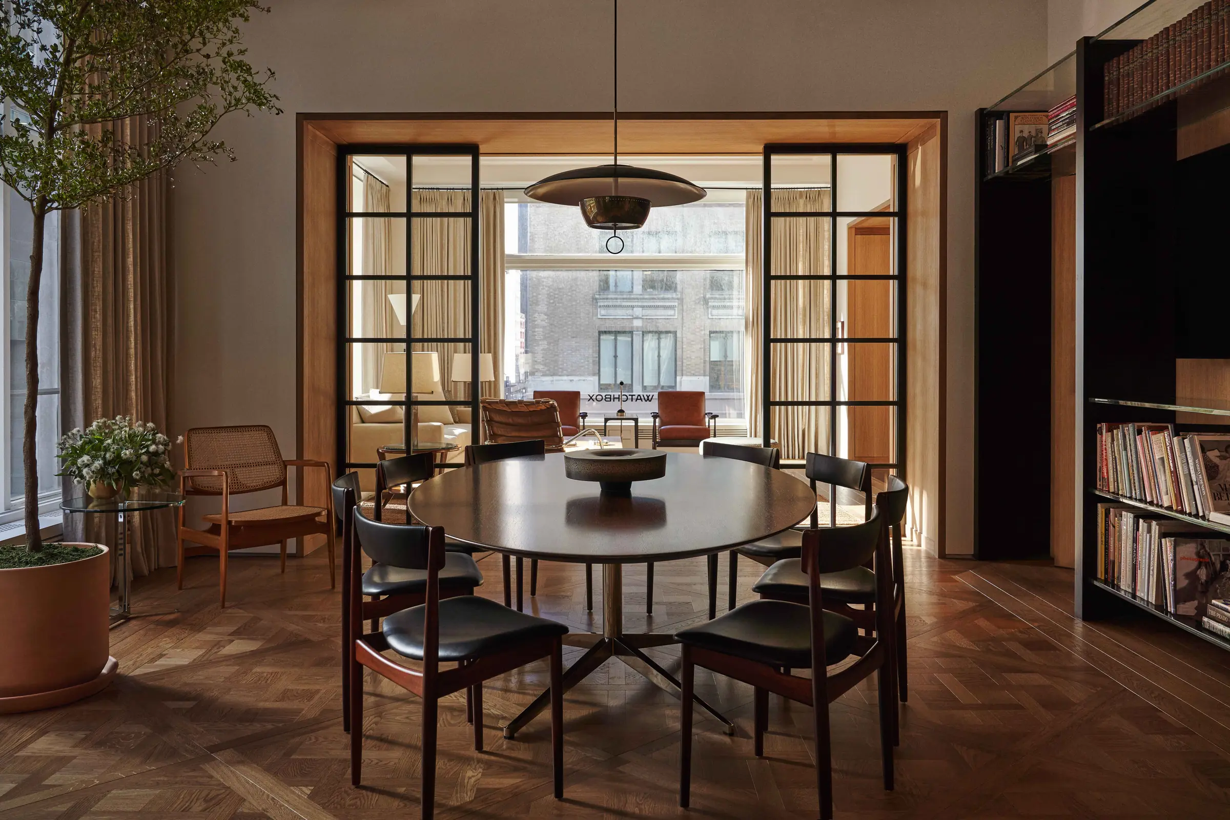 Interior dining room with oval table, leather chairs, herringbone floor and glass doors to a lounge, for WatchBox.