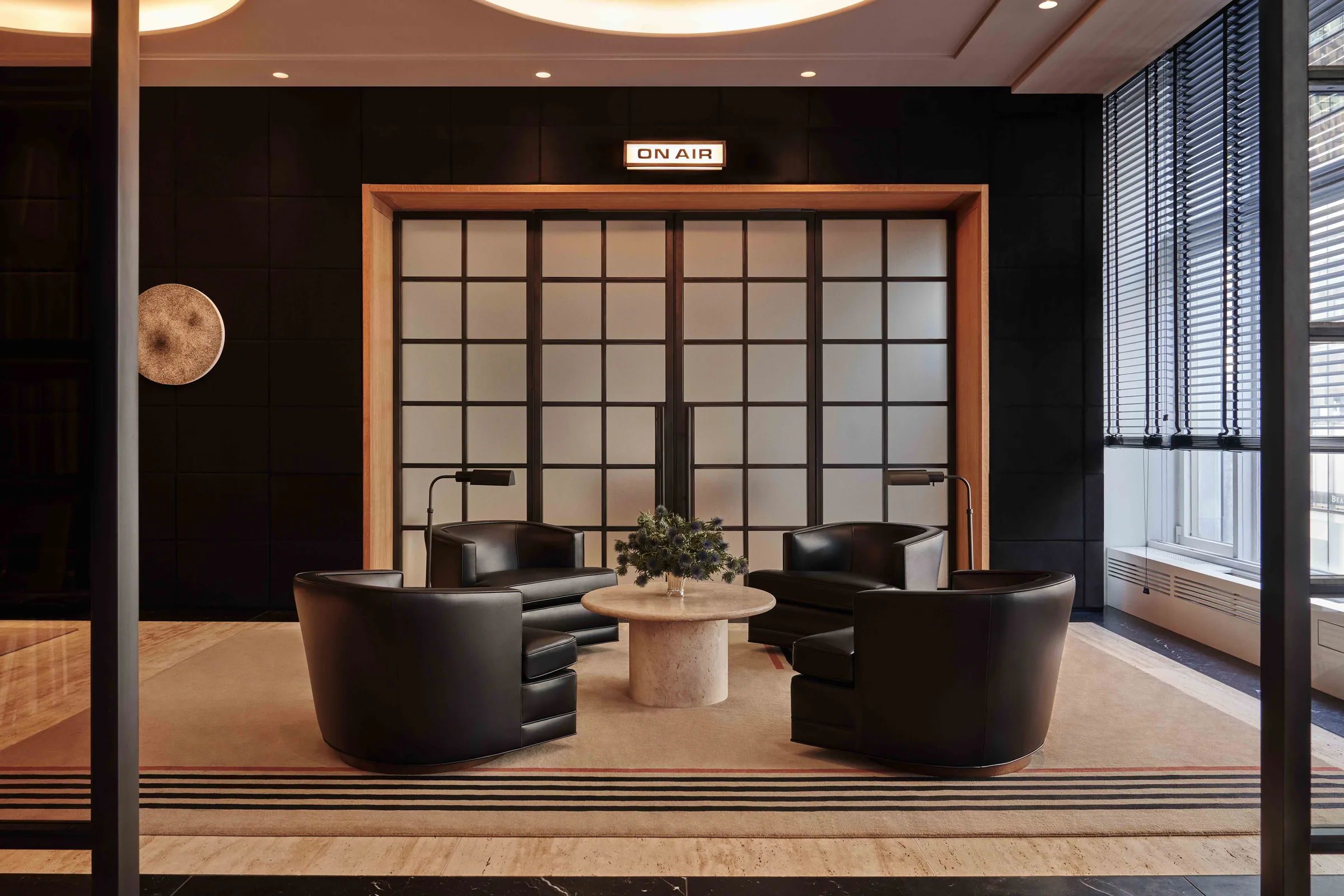 Interior lounge with four black leather armchairs, a stone table and frosted glass doors under an On Air sign, for WatchBox.