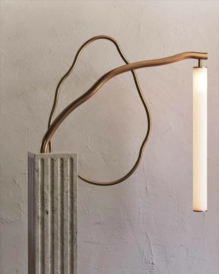 Sculptural brass floor lamp with looping arms and a glowing tube on a fluted travertine base, against plaster, for Anna Karlin.
