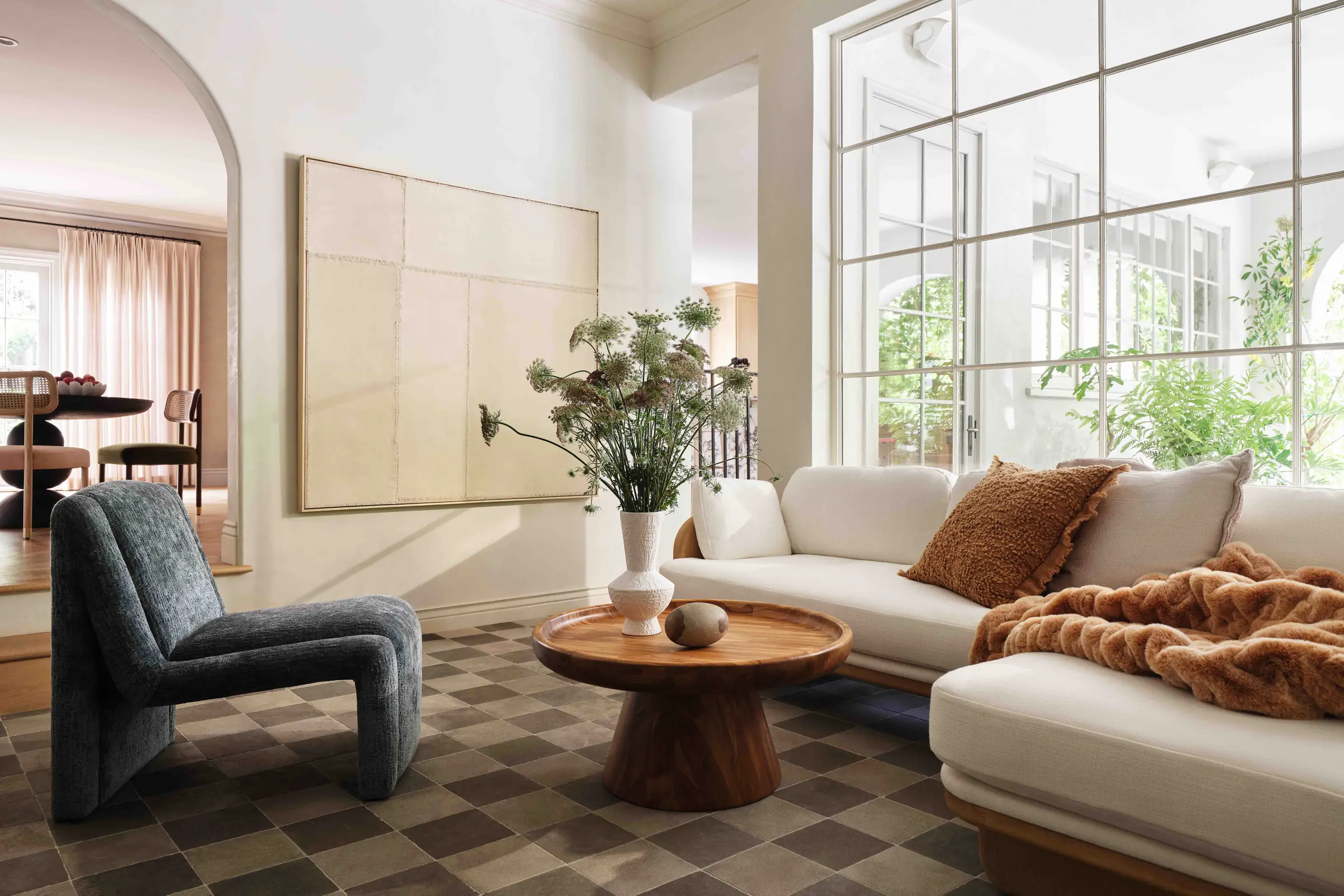 Living room with curved cream sofa, grey lounge chair, round wood coffee table and checkered floor, for Anthropologie.