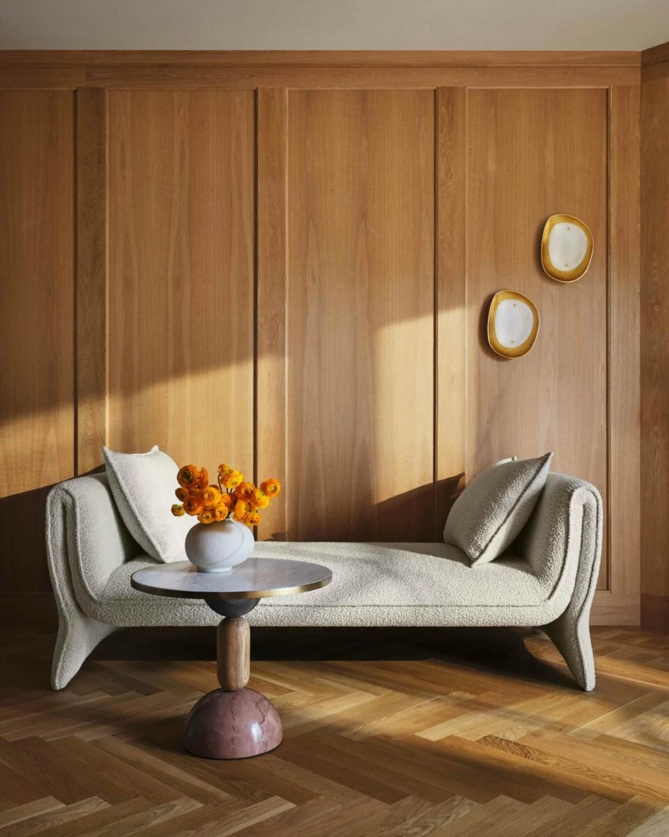 Cream bouclé daybed with side table and orange ranunculus against oak paneling on herringbone floor, for Anthropologie.