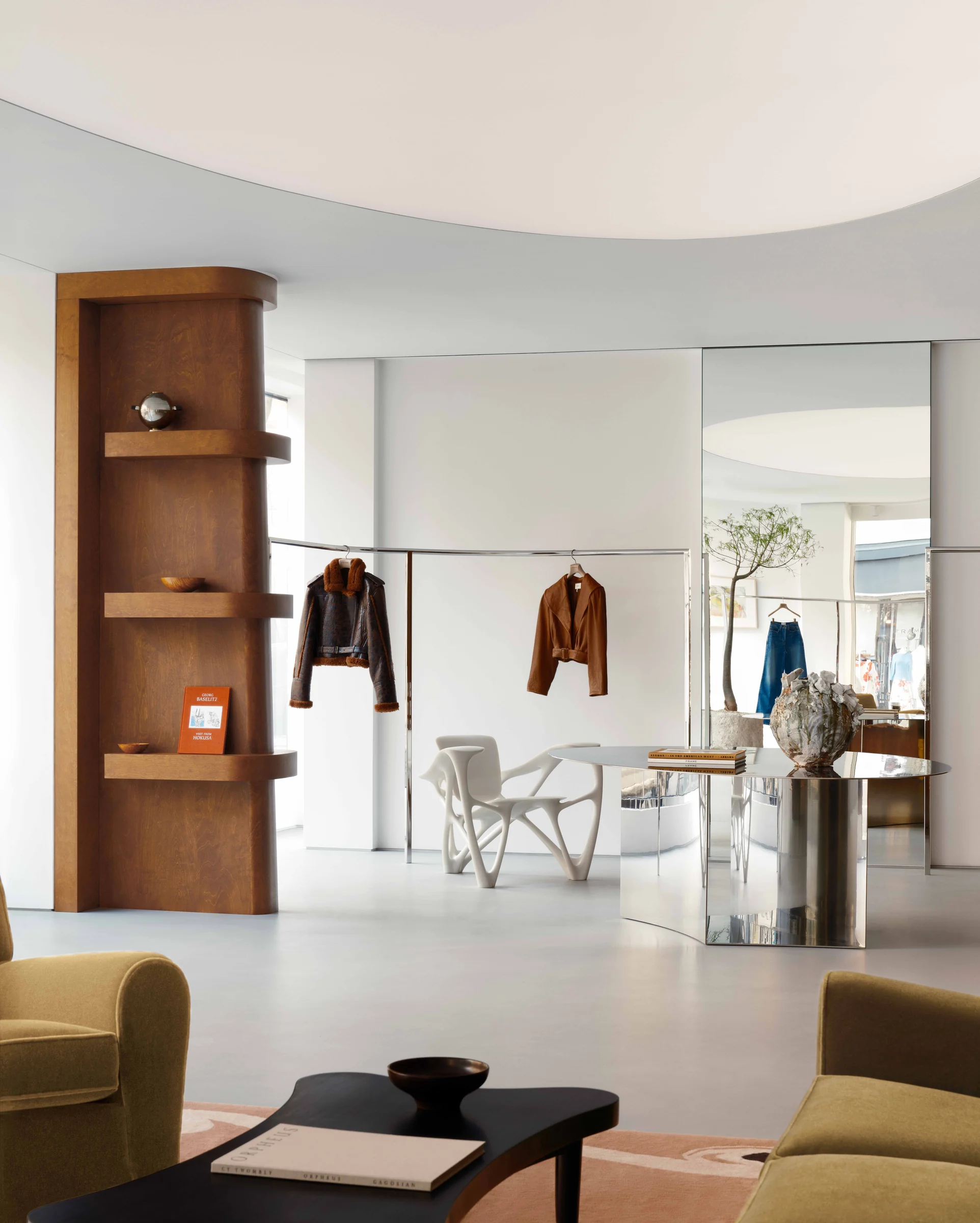 Boutique interior with jackets on chrome rails, oak shelving, mirrored table and olive armchairs, for Frame.