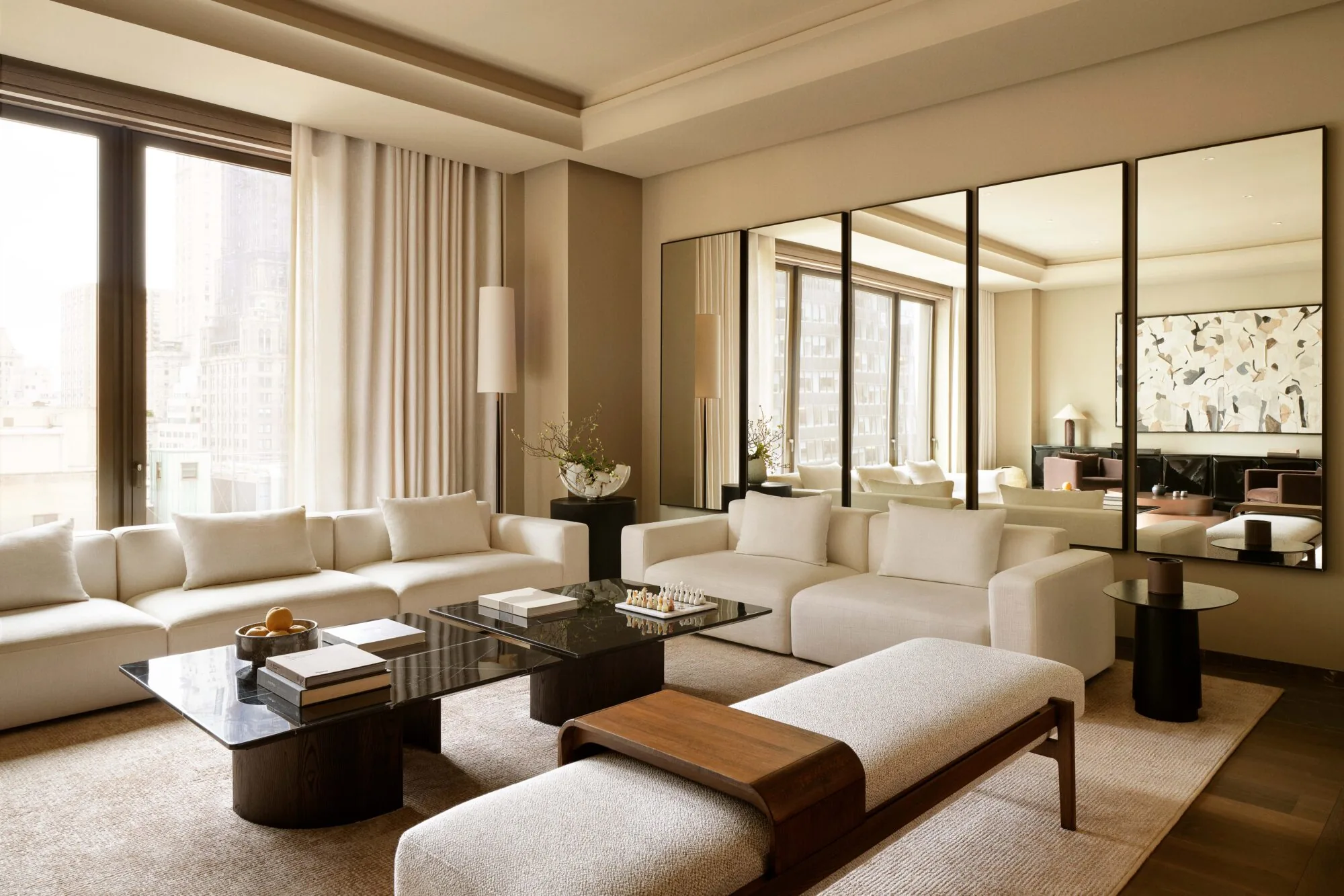 Hotel suite living room with cream sofas, black marble coffee tables, mirrored wall and city view windows, for Aman.